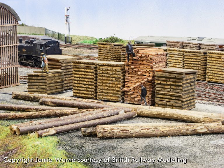 Stacks of sleepers and logs in the Redbridge works yard, with a steam locomotive shunting behind