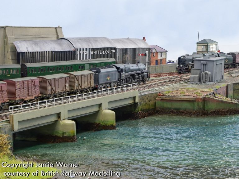 Steam-hauled goods train crossing the river bridge in front of the works buildings